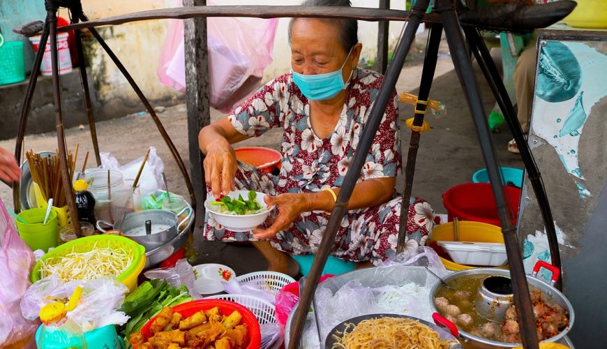 Banh tam bi is often regarded as a popular street food dish in the Mekong Delta, Vietnams rice basket, because of its delicious and appealing taste. On a tour of An Giang that borders Cambodia, dont forget to visit this stall located near Long Hung crosscroads in Tan Chau Town where an old woman has been serving this dish on her shoulder pole. Without a signboard, advertising or table, her stall has been going strong for more than 20 years.